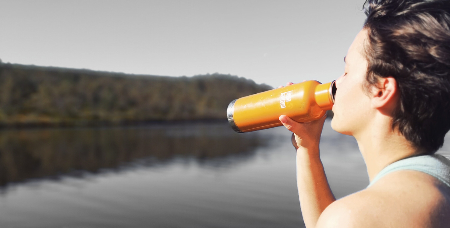 Woman drinking flask of water at lake