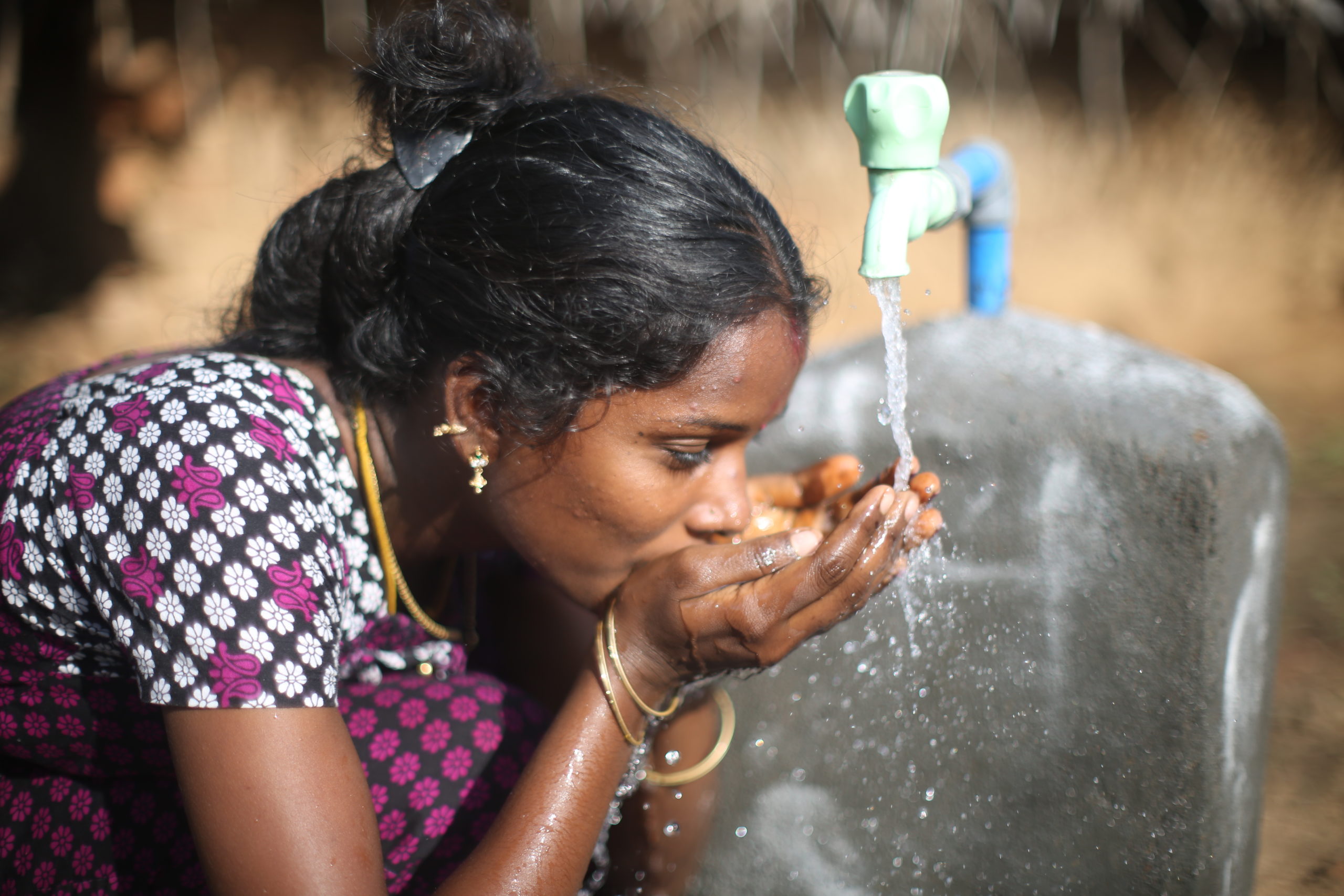 Woman drinking water from her hands flowing out of a pump